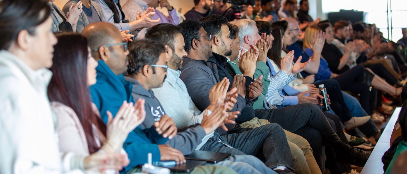 Employees seated in an auditorium applauding during an indoor presentation.